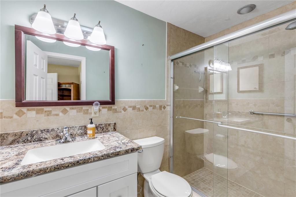 A bathroom features a granite vanity, a white toilet, and a glass-enclosed walk-in shower — 704 GREEN ROAD, NEW SMYRNA BEACH, FL