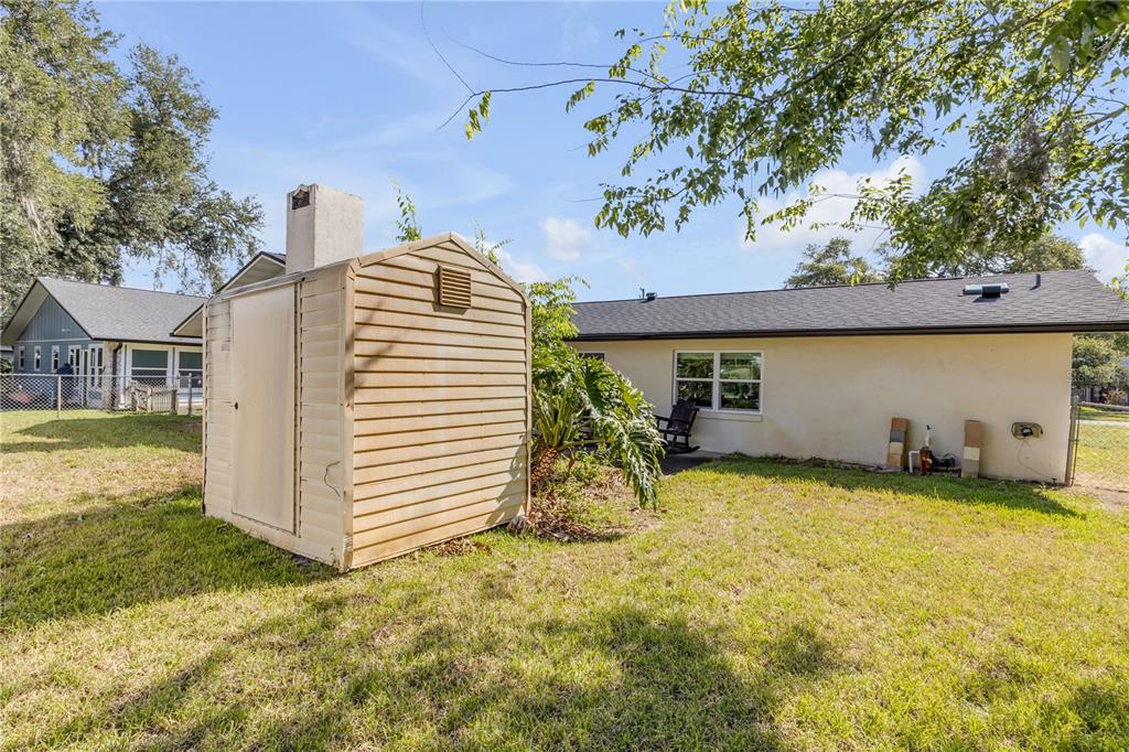 A beige storage shed stands in a grassy backyard next to a single-story house — 704 GREEN ROAD, NEW SMYRNA BEACH, FL