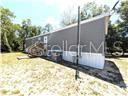 An exterior view of a gray manufactured home with white skirting on a grassy lot — 5416 W COUGAR LANE, DUNNELLON, FL