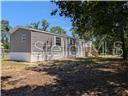 A single-story manufactured home with gray siding sits on a dirt lot with trees — 5416 W COUGAR LANE, DUNNELLON, FL