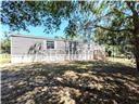A single-story manufactured home with a wooden deck stands in a grassy, tree-filled yard — 5416 W COUGAR LANE, DUNNELLON, FL