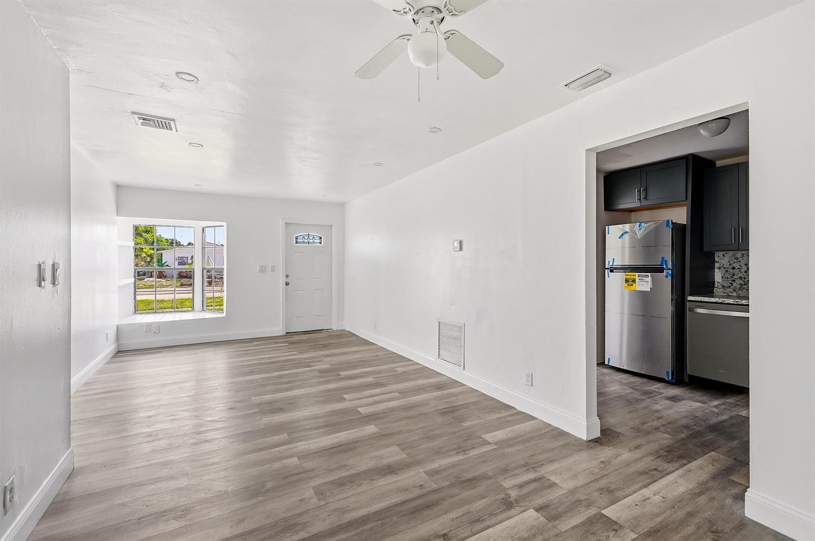 A living room with light wood-look flooring, white walls, a ceiling fan, and an adjacent kitchen — 1060 SW 5th Terrace, Deerfield Beach FL 33441, DEERFIELD BEACH, FL