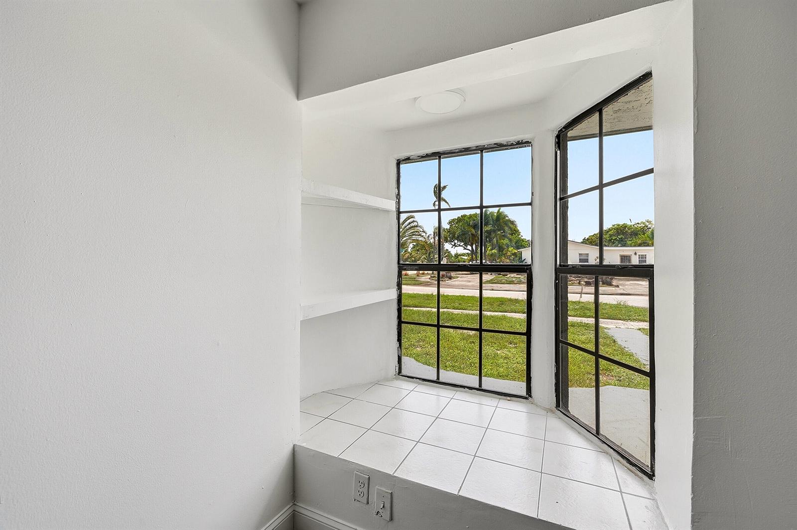 A tiled window nook features built-in white shelves and black-framed windows overlooking a grassy yard — 1060 SW 5th Terrace, Deerfield Beach FL 33441, DEERFIELD BEACH, FL