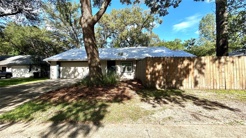 A single-story house with a metal roof, a wooden privacy fence, and a large tree — 1034 SW 79TH TERRACE, GAINESVILLE, FL