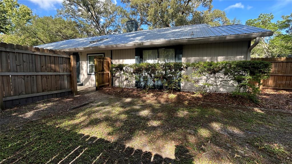 A single-story house exterior features a metal roof, light siding, and a fenced backyard area — 1034 SW 79TH TERRACE, GAINESVILLE, FL