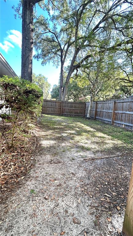A sandy backyard area features a wooden fence and large trees under a blue sky — 1034 SW 79TH TERRACE, GAINESVILLE, FL