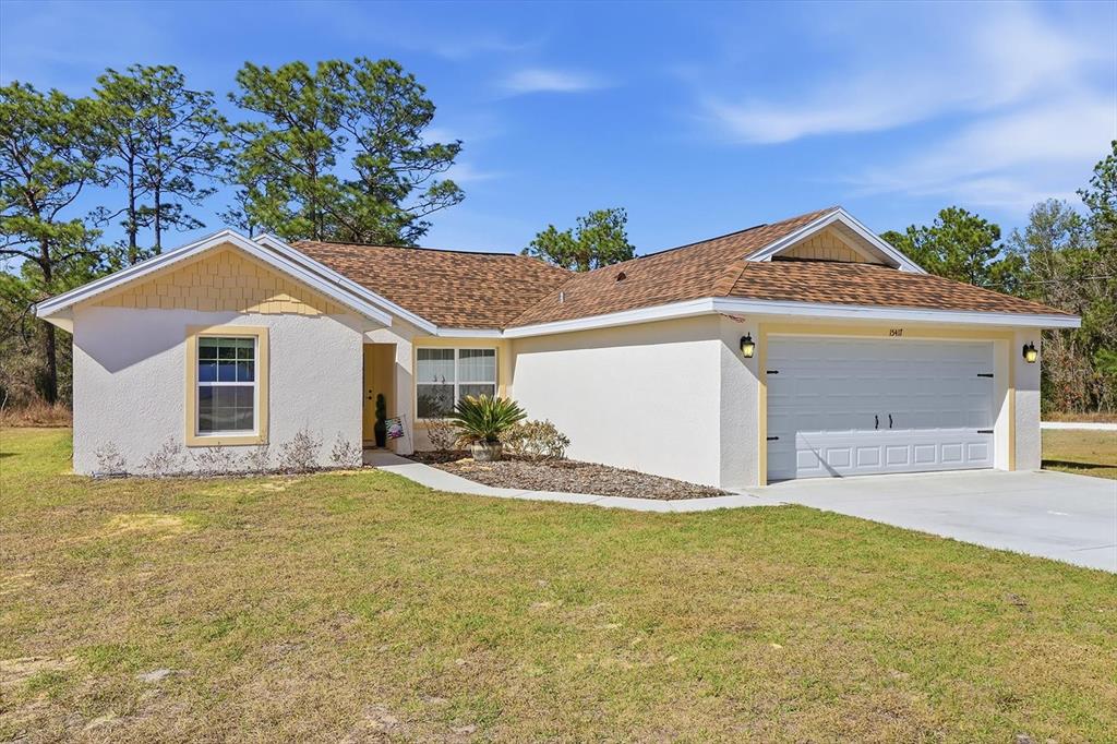 A single-story house with a white stucco exterior, brown shingle roof, and a two-car garage — 15417 COOT ROAD, BROOKSVILLE, FL