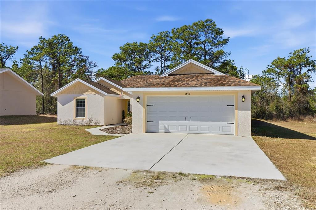 A single-story house with a white garage door, tan stucco siding, and a shingled roof — 15417 COOT ROAD, BROOKSVILLE, FL