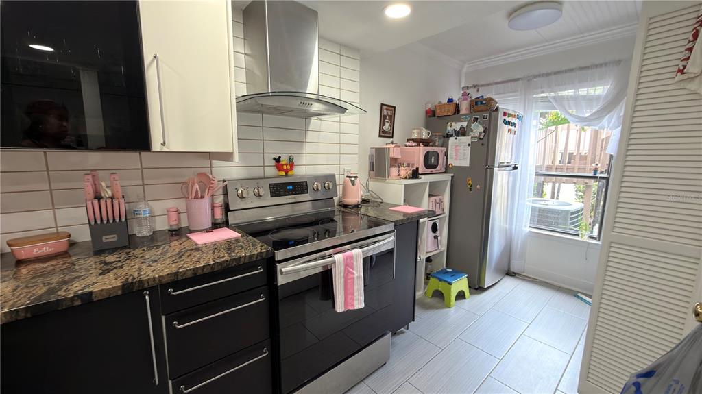 A kitchen features black cabinets, granite countertops, stainless steel appliances, and pink decorative accents — 5308 JASMINE CREEK LANE UNIT 1308A, ORLANDO, FL