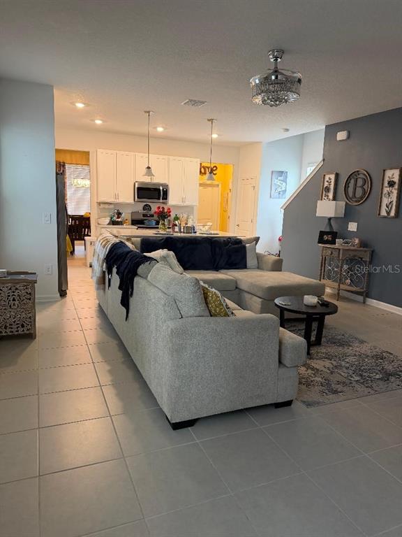 An open-concept living room features a large gray sectional sofa facing a kitchen with white cabinets — 1892 BRIGHT SKY DRIVE, KISSIMMEE, FL