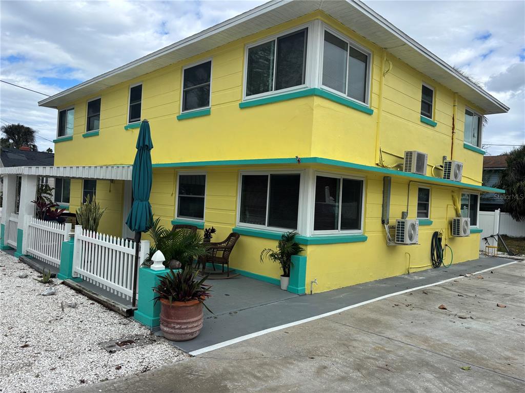 A two-story yellow building with teal trim features a white picket fence and patio area — 8301 W GULF BOULEVARD, TREASURE ISLAND, FL