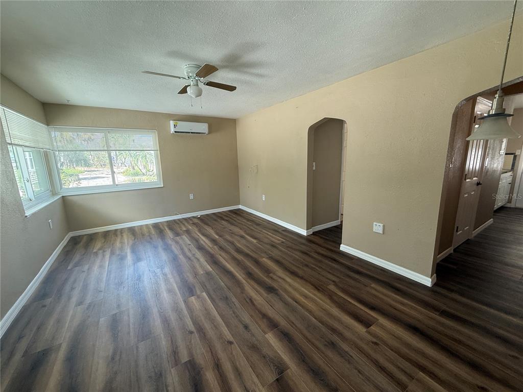 An empty living room features wood-look flooring, a ceiling fan, and a wall-mounted air conditioner — 8301 W GULF BOULEVARD, TREASURE ISLAND, FL