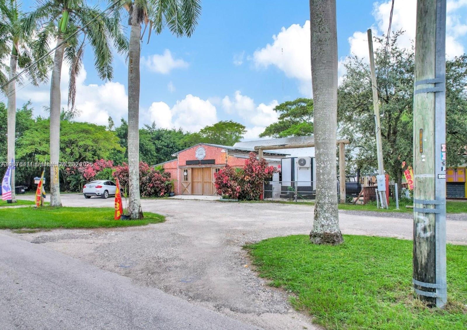 A red brick building with wooden double doors sits on a gravel lot with palm trees — 17480 SW 232nd St, Miami FL 33170, MIAMI, FL