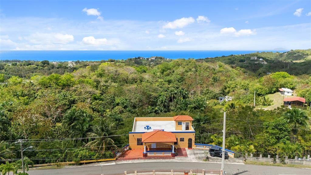 An aerial view shows a two-story yellow house with a red tile roof and ocean views — Km 15 H 7 PR 115 VILLA LA JOLLA, RINCON, PR