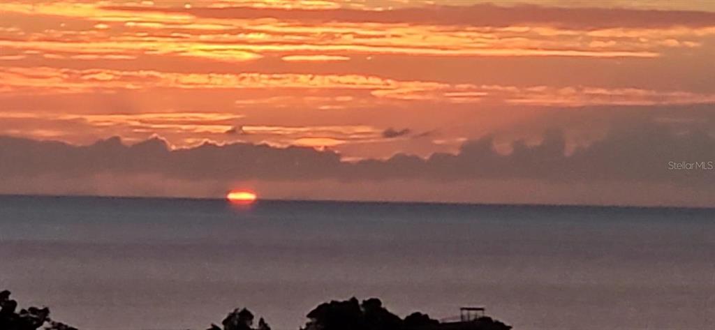 A bright orange sunset glows over the ocean horizon above a dark, silhouetted landscape — Km 15 H 7 PR 115 VILLA LA JOLLA, RINCON, PR