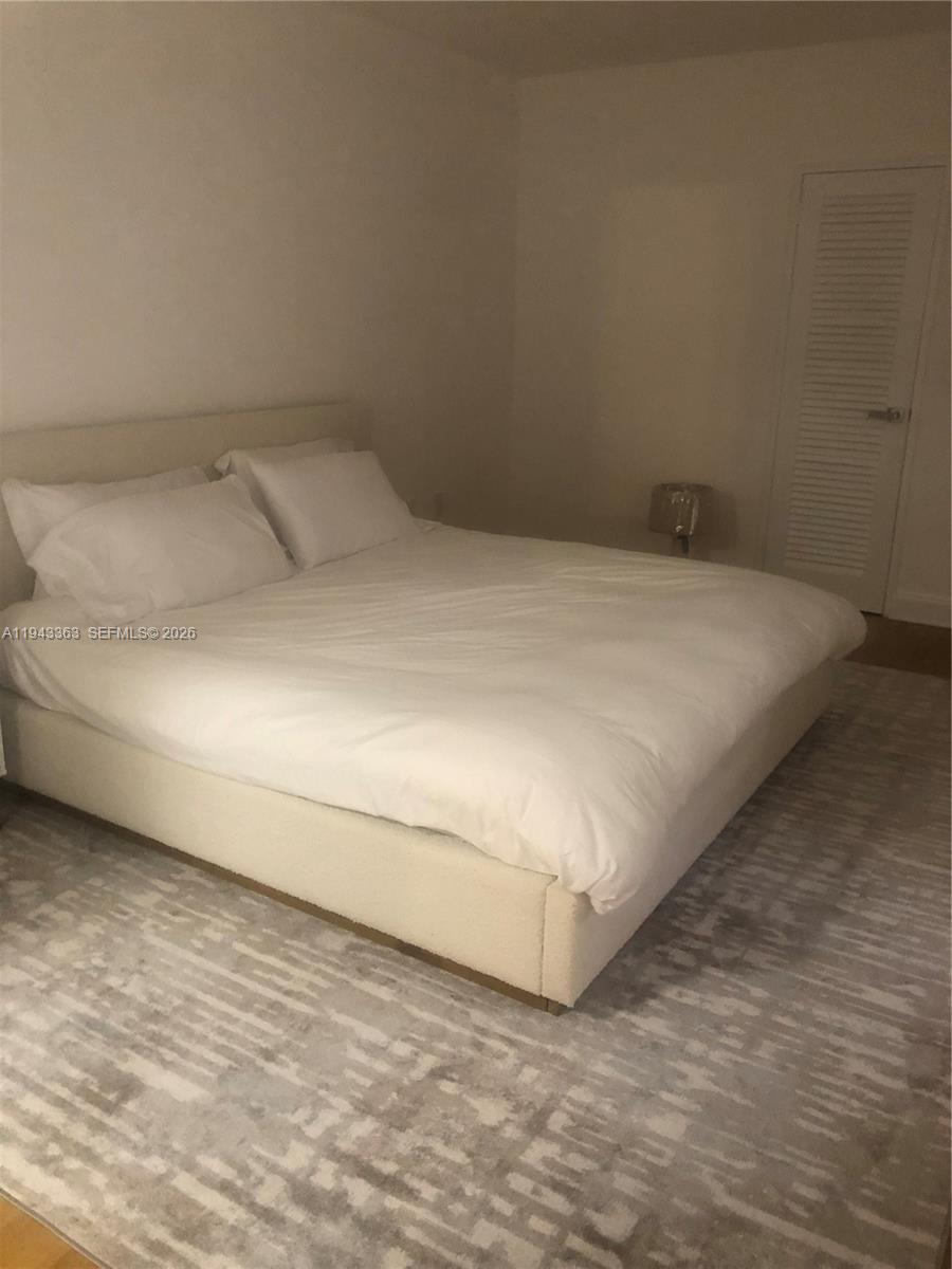A bedroom features a large white bed on a patterned rug near a closet door — 10185 Collins Ave # 1016, Bal Harbour FL 33154, BAL HARBOUR, FL
