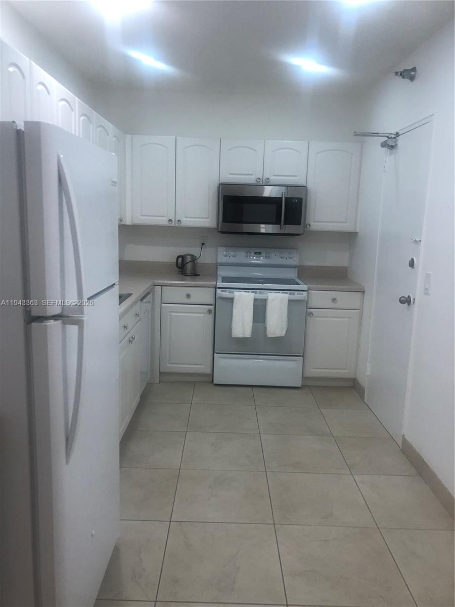 A kitchen features white cabinets, stainless steel appliances, and light-colored tile flooring — 10185 Collins Ave # 1016, Bal Harbour FL 33154, BAL HARBOUR, FL