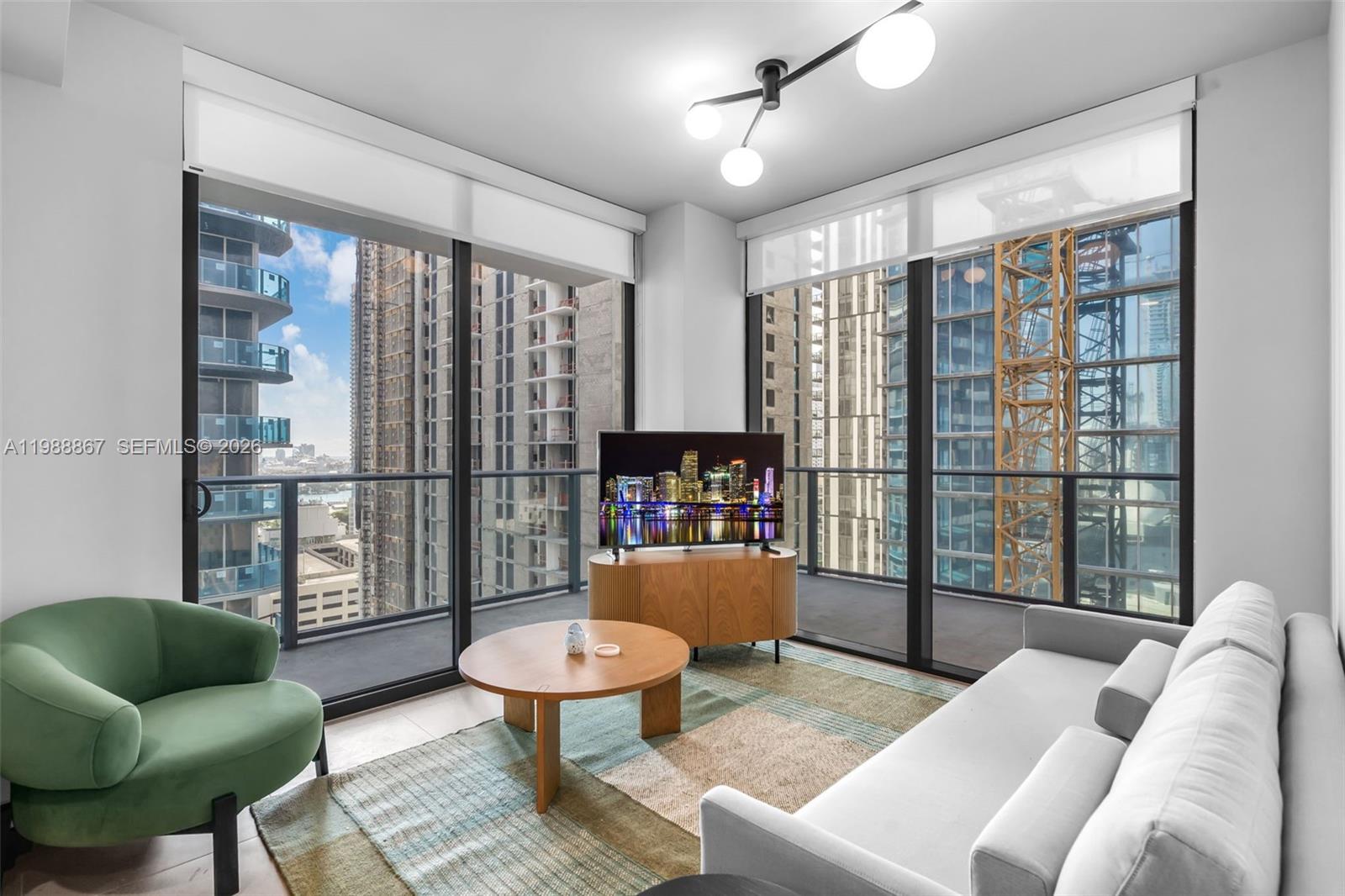 A modern living room features floor-to-ceiling windows, a green armchair, and a light-colored sofa — 11 NE 6th # 2207, Miami FL 33131, MIAMI, FL