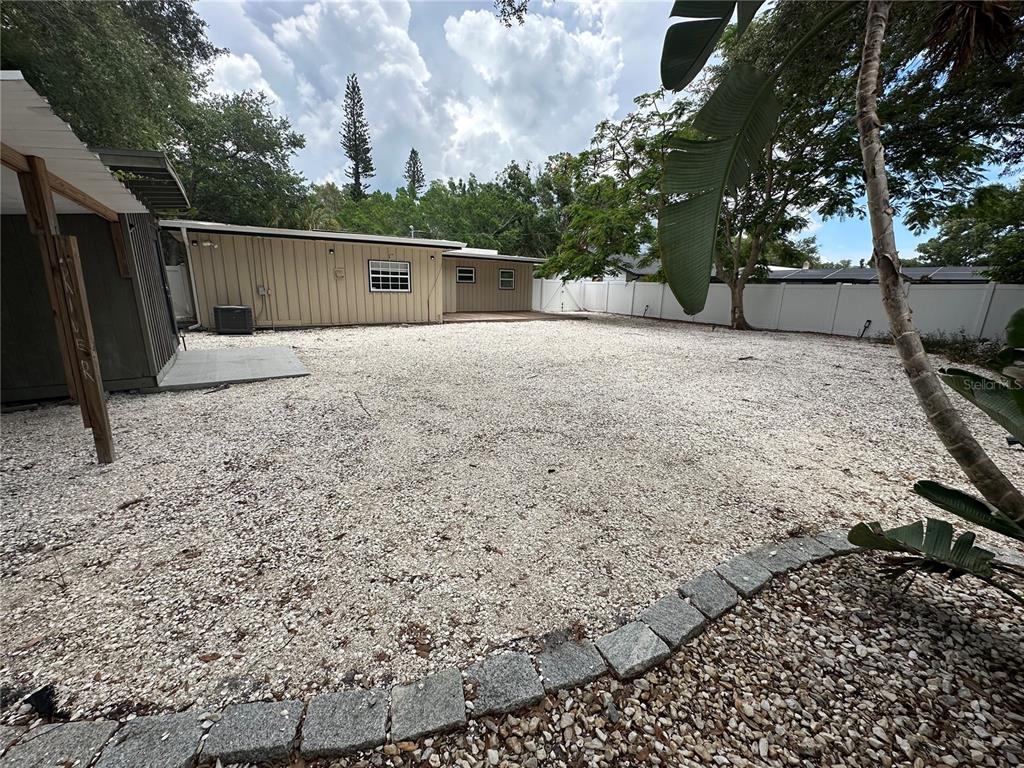 A large backyard features a gravel ground cover, a tan house, and a white fence — 2559 E PAULSTAN COURT, SARASOTA, FL