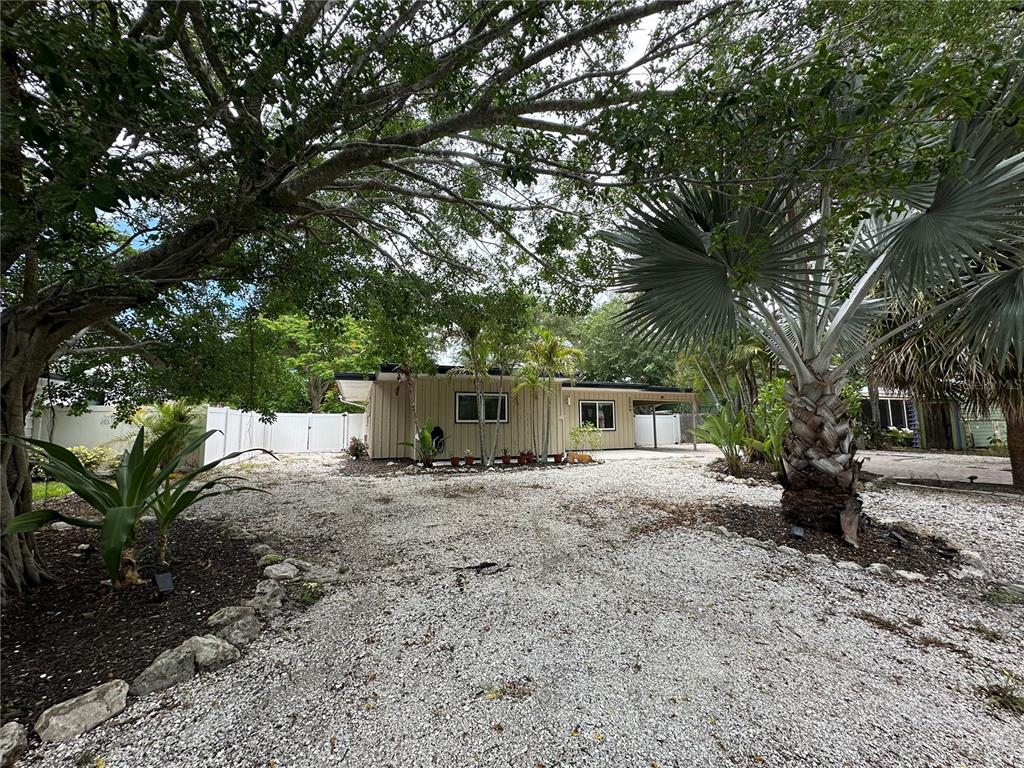 A single-story house with light-colored siding sits behind a large gravel driveway and trees — 2559 E PAULSTAN COURT, SARASOTA, FL