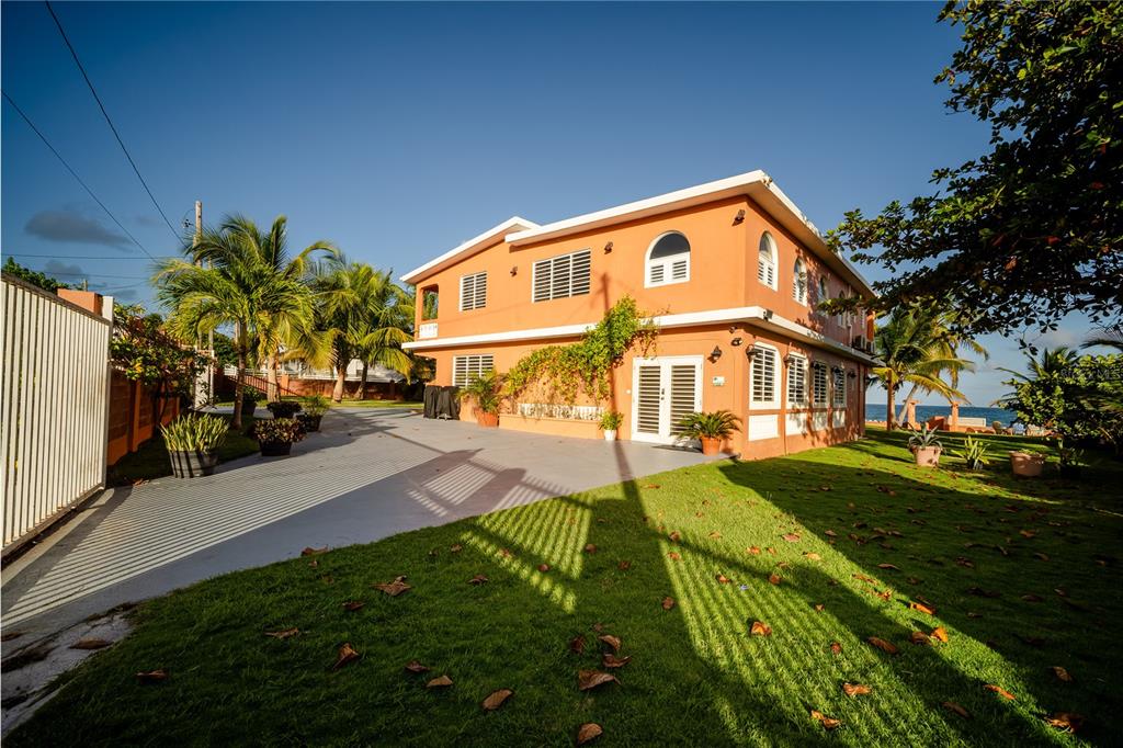 An orange two-story house with a paved driveway and lawn sits near the ocean — Parcela #10 BARRIO CAMINO NUEVO, YABUCOA, PR