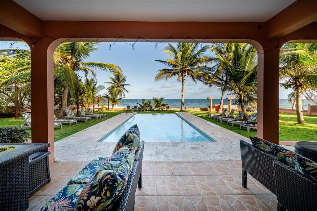 A covered patio overlooks a rectangular swimming pool, palm trees, and the ocean beyond — Parcela #10 BARRIO CAMINO NUEVO, YABUCOA, PR