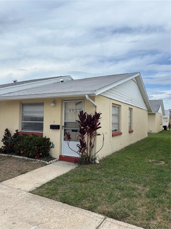 A single-story yellow stucco house with a white storm door and a small front garden — 4923 GETNER STREET, NEW PORT RICHEY, FL