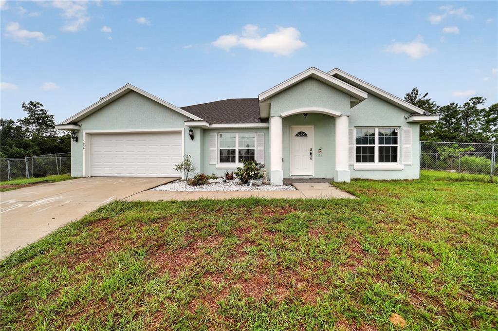 A single-story, light green stucco house with a two-car garage and a covered front porch — 3050 SW 177TH PLACE ROAD, OCALA, FL