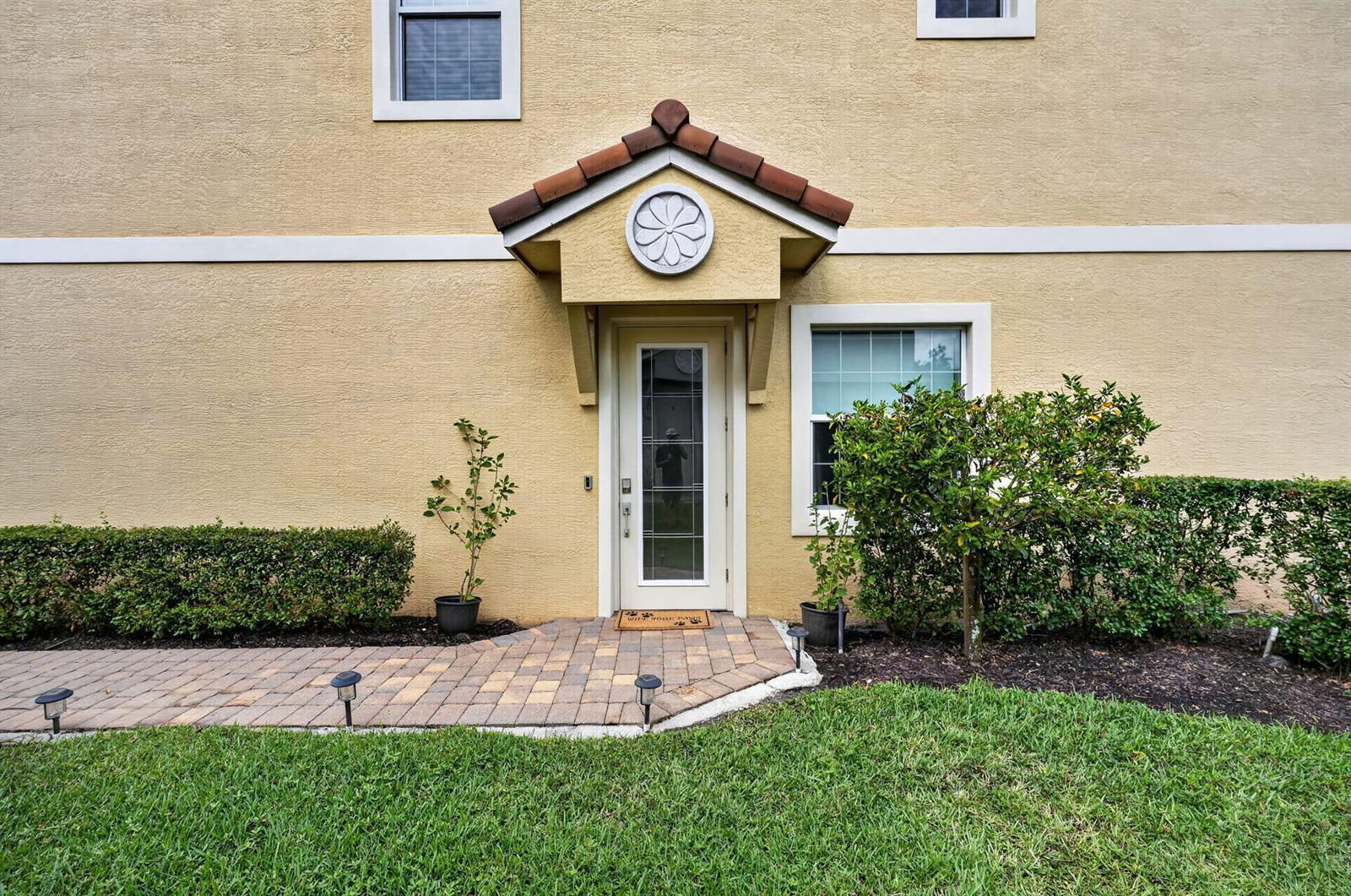 A tan stucco building exterior features a covered entryway with a tiled roof and door — 615 SW Glen Crest Way, Stuart FL 34997, STUART, FL