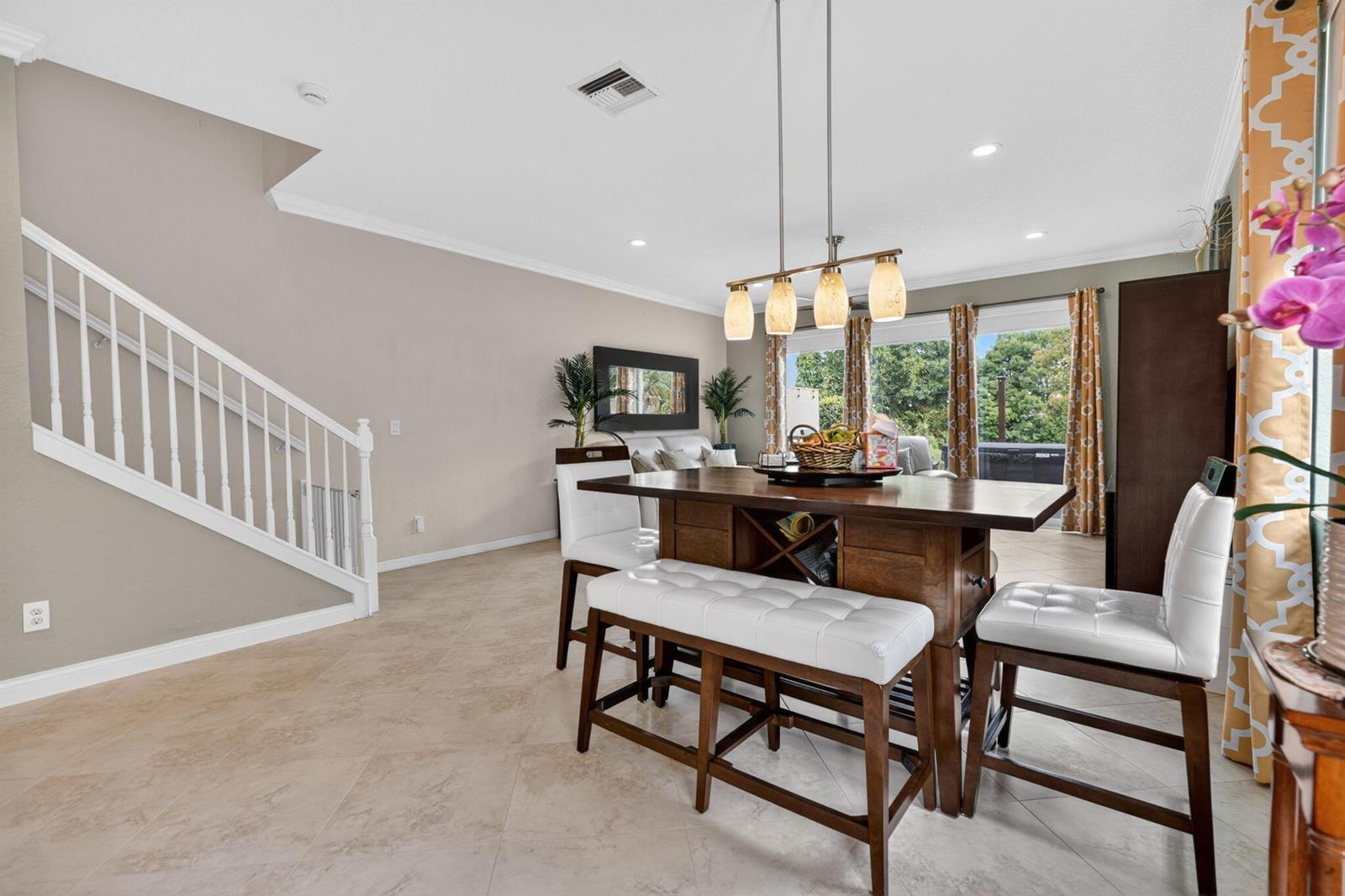 A dining area features a wooden table with white stools, tile floors, and a staircase — 615 SW Glen Crest Way, Stuart FL 34997, STUART, FL