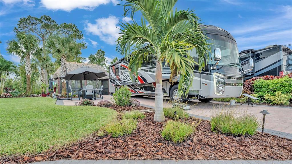 A large recreational vehicle is parked on a paved lot next to a tiki hut — 3244 FISH HAWK DRIVE, POLK CITY, FL