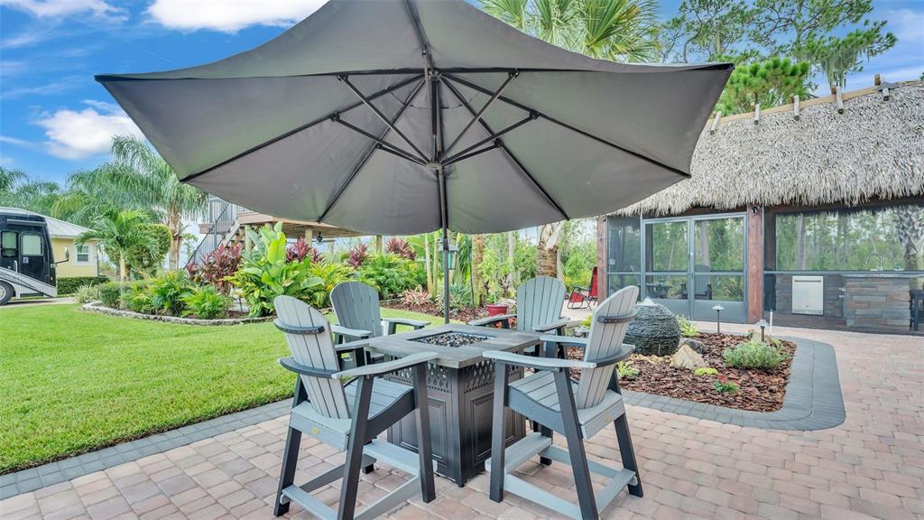 A patio features a fire pit table with four chairs under a large gray umbrella — 3244 FISH HAWK DRIVE, POLK CITY, FL