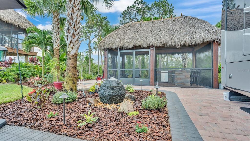 A thatched-roof tiki hut with a screened-in outdoor kitchen sits beside a landscaped garden — 3244 FISH HAWK DRIVE, POLK CITY, FL