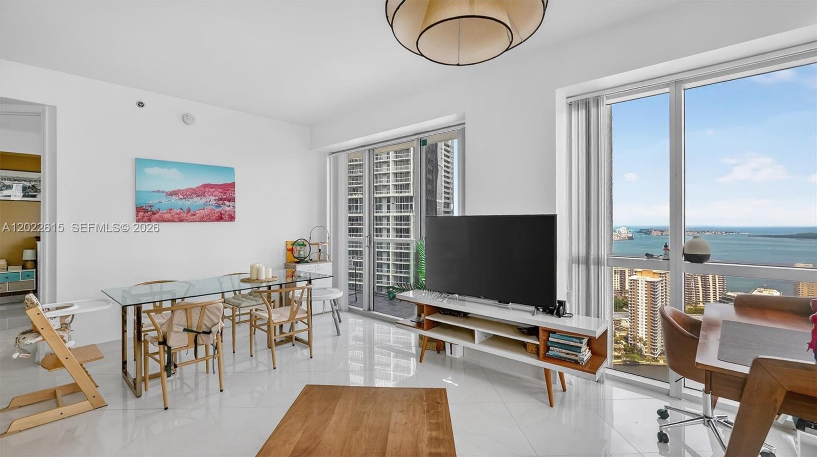 A bright living and dining area features white tile floors, a glass table, and ocean views — 500 Brickell Ave # 4102, Miami FL 33131, MIAMI, FL