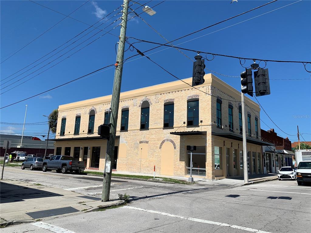 A two-story tan brick building stands on a street corner under a clear blue sky — 2100 W MAIN STREET, TAMPA, FL