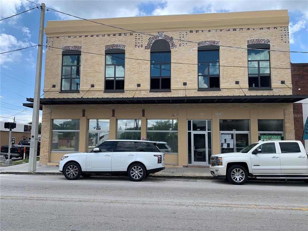 A two-story brick commercial building with large windows and two white SUVs parked in front — 2100 W MAIN STREET, TAMPA, FL