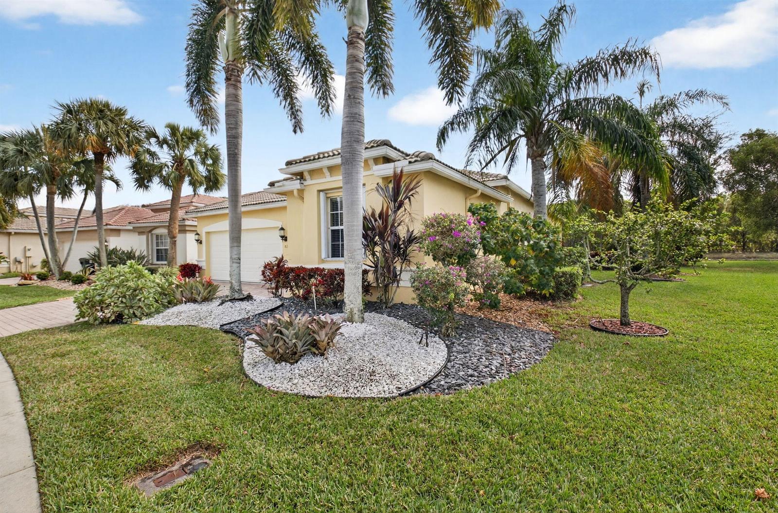 A single-story house with a yellow stucco exterior, palm trees, and landscaped rock beds — 8208 Parini Way, Lake Worth FL 33467, LAKE WORTH, FL