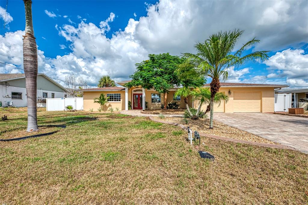 A single-story house with a tan exterior, red front door, and a paved driveway — 1962 ARKANSAS AVENUE, ENGLEWOOD, FL