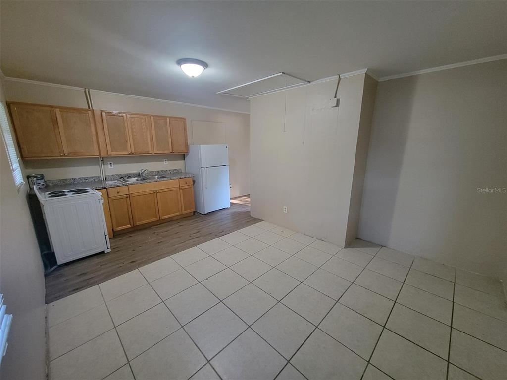 A kitchen features light wood cabinets, white appliances, and a mix of tile and wood flooring — 729 E CAROLINA AVENUE, DELAND, FL