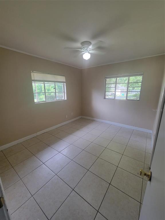 An empty bedroom features beige walls, white tile flooring, and a ceiling fan — 729 E CAROLINA AVENUE, DELAND, FL