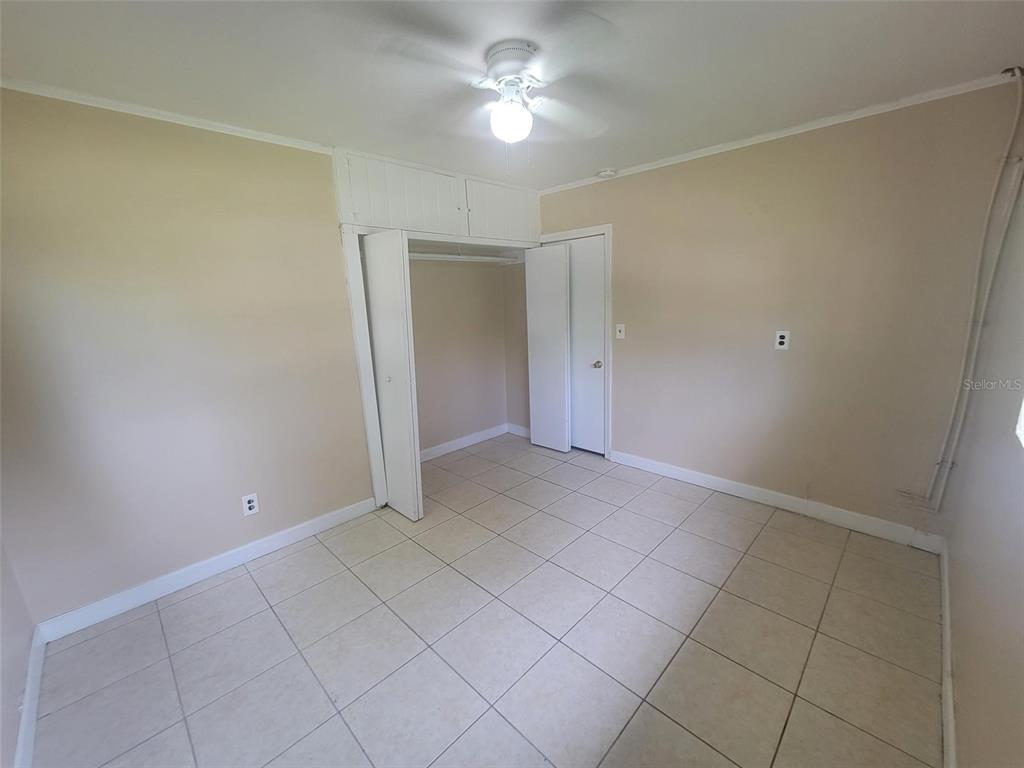 A bedroom with beige walls, light-colored floor tiles, a ceiling fan, and a built-in closet — 729 E CAROLINA AVENUE, DELAND, FL