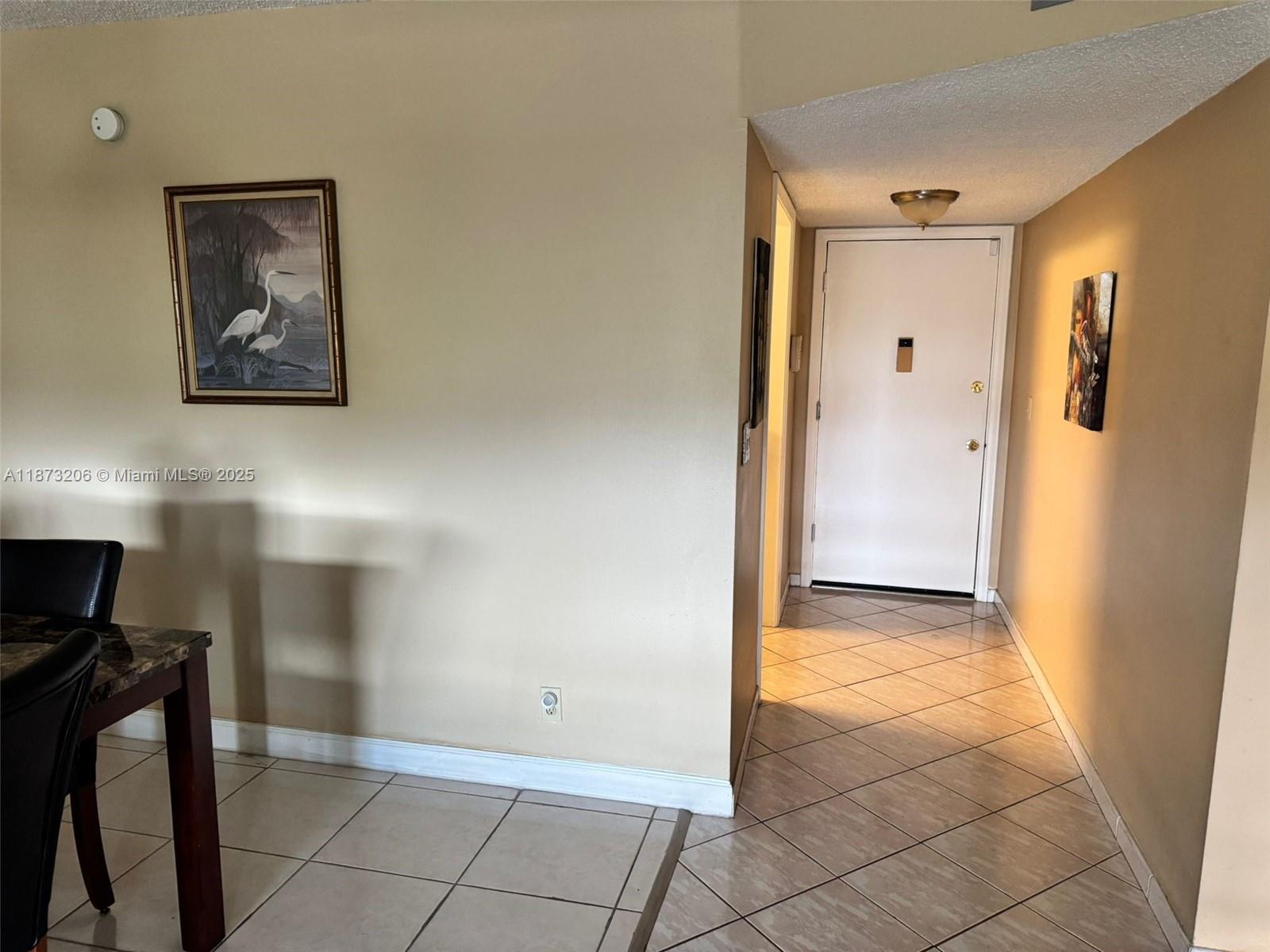 A dining area with tiled floors leads to a hallway with a white entry door — 2061 NW 47th Ter # 407, Lauderhill FL 33313, LAUDERHILL, FL