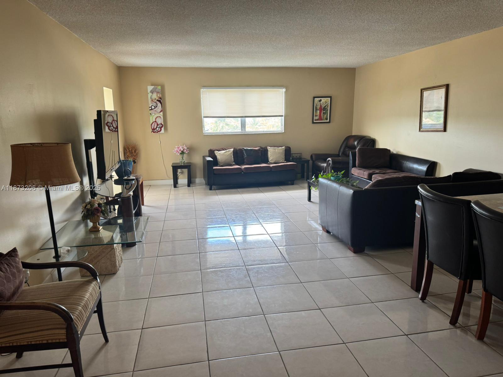 A living room features light-colored tile flooring, beige walls, and a brown sofa set — 2061 NW 47th Ter # 407, Lauderhill FL 33313, LAUDERHILL, FL