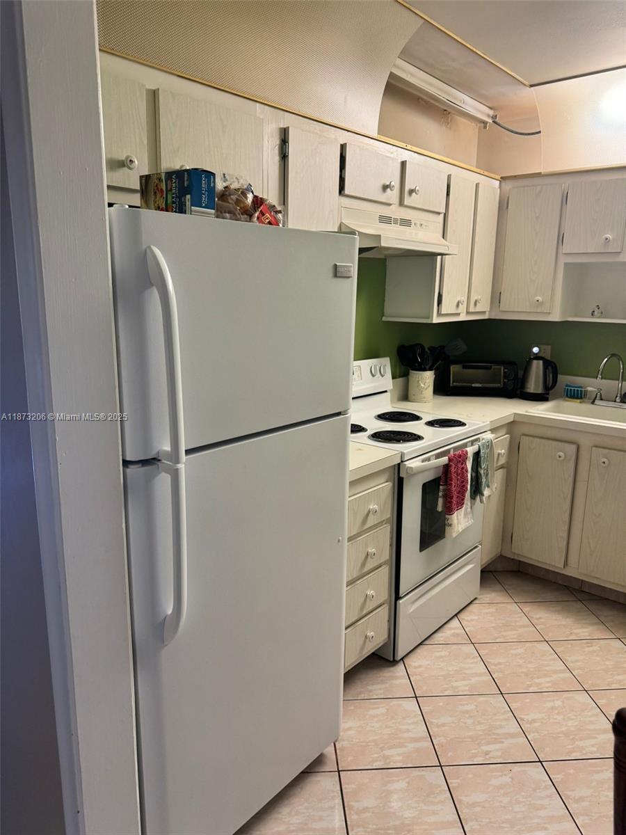 A kitchen features white appliances, light-colored wooden cabinets, a green backsplash, and tiled flooring — 2061 NW 47th Ter # 407, Lauderhill FL 33313, LAUDERHILL, FL
