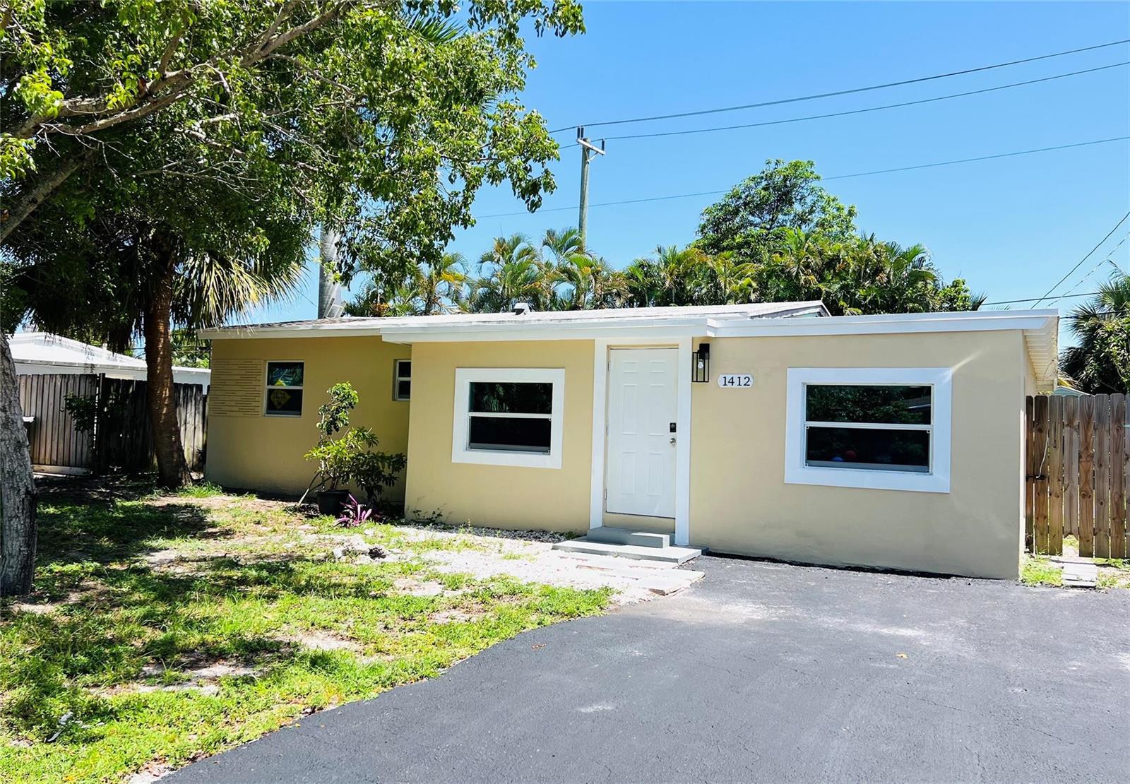 A single-story yellow house with a white door and driveway under a clear blue sky — 1412 NE 25th Court, Pompano Beach FL 33064, POMPANO BEACH, FL