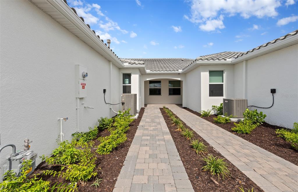A paved walkway leads to a recessed entryway between two white stucco building wings — 27108 CLAM SHELL COURT, ENGLEWOOD, FL