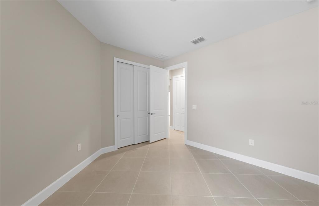 An empty room with beige walls, light tile flooring, and white interior doors — 27108 CLAM SHELL COURT, ENGLEWOOD, FL
