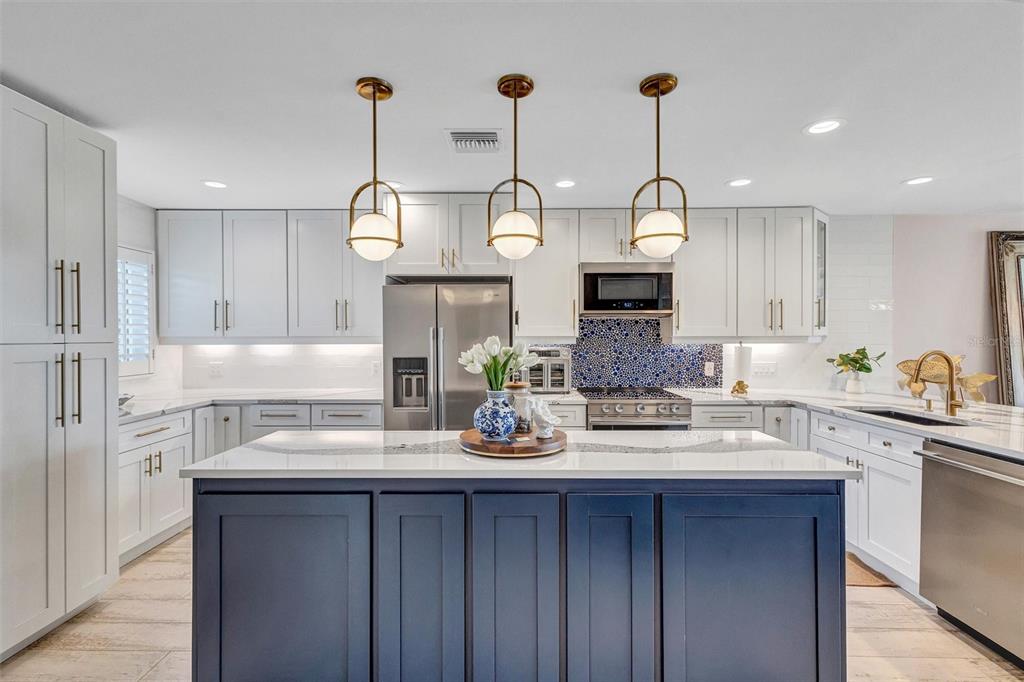 A kitchen features white cabinetry, a dark blue island, and three gold pendant lights — 7125 GULF OF MEXICO DRIVE UNIT 22, LONGBOAT KEY, FL