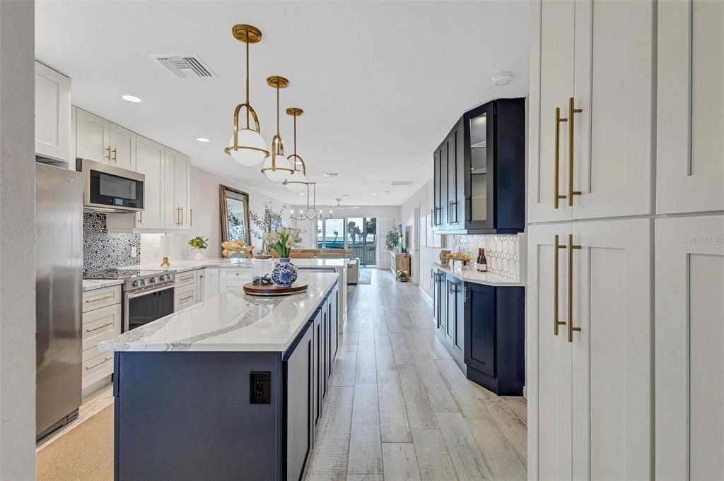 A modern kitchen features a blue island, white cabinets, gold hardware, and wood-look tile flooring — 7125 GULF OF MEXICO DRIVE UNIT 22, LONGBOAT KEY, FL