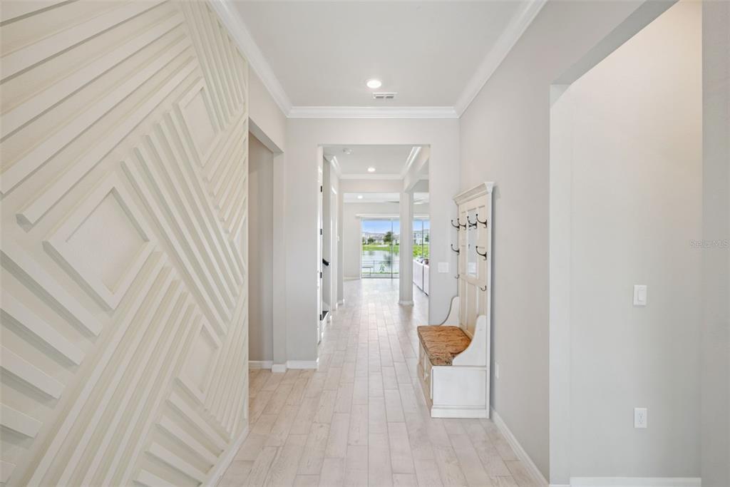 A bright hallway features light wood-look tile floors, a textured accent wall, and a coat rack — 13871 DESTIN BEACH LANE, ORLANDO, FL